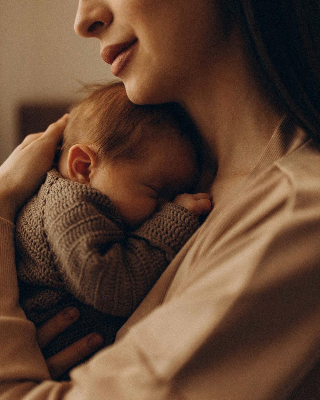 A mother gently holding her baby close to her chest, with soft lighting. This image is the cover for a blog post on Journal prompts for moms.