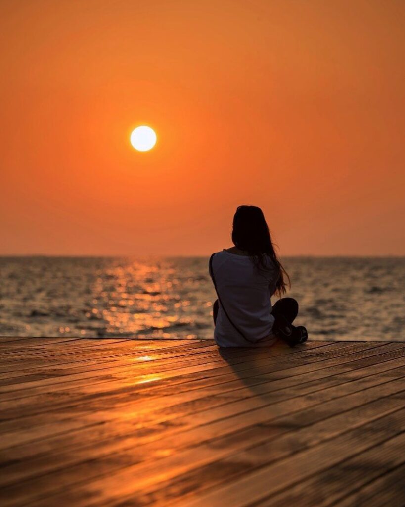 Person from behind, sitting by a calm lake, embodying the power of silence.