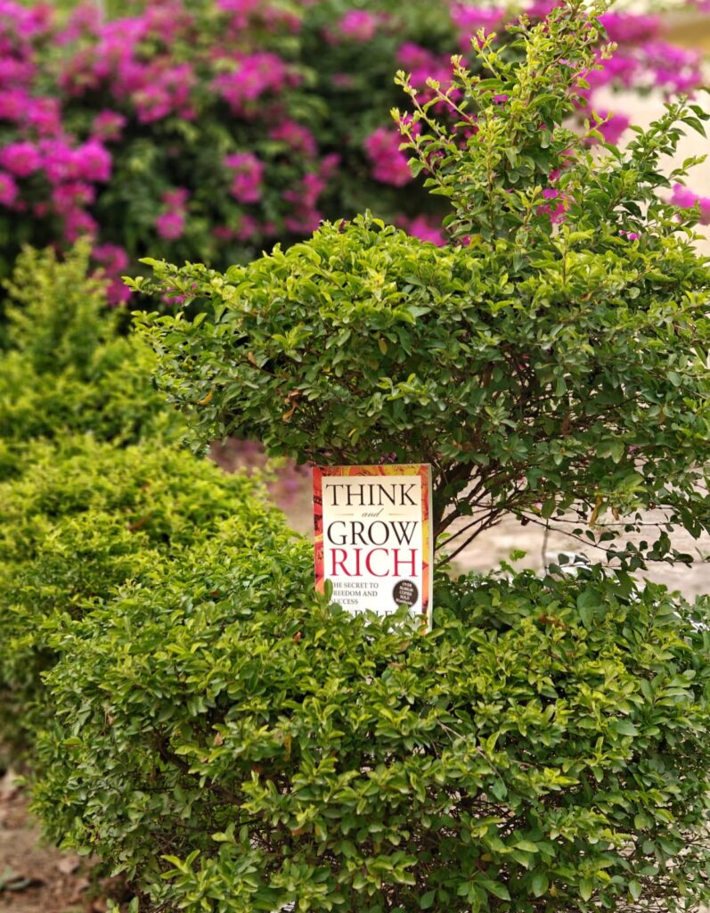 "Think and Grow Rich" book in the midst of a lush green garden.